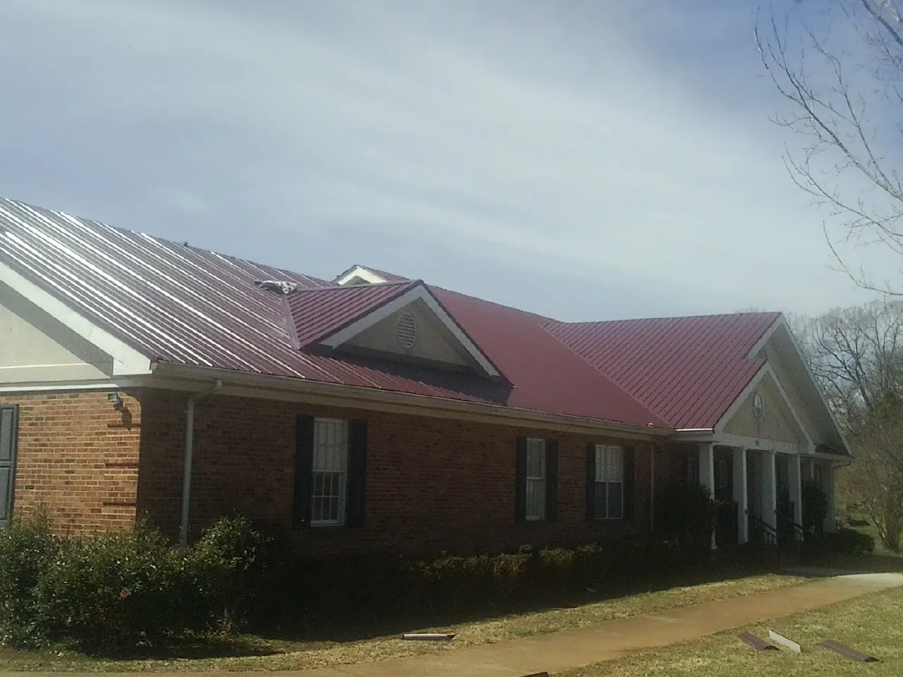 Red metal roof with gabled entries on a long brick building, from a Hail Damage Roof Repair job in Pennsville