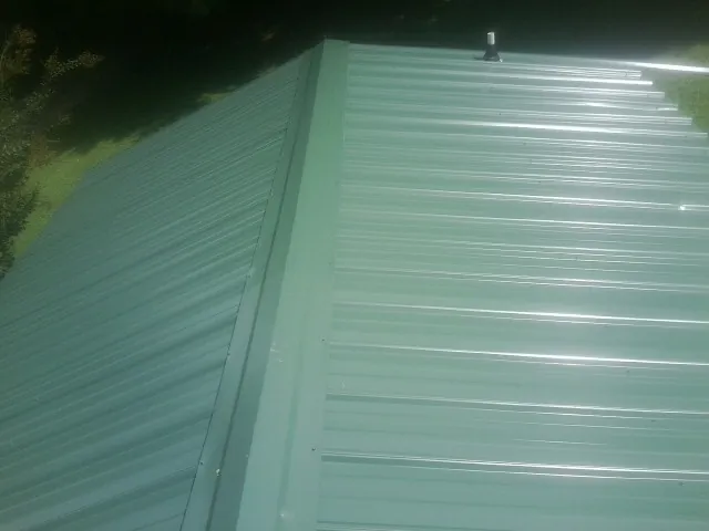 New green metal panels meeting at the ridge of a roof — Flat Roof Repair work by our crew in Pennsville