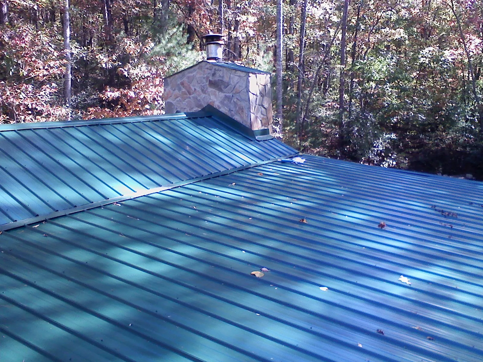 New green metal roof and stone chimney surrounded by autumn woods in Pennsville