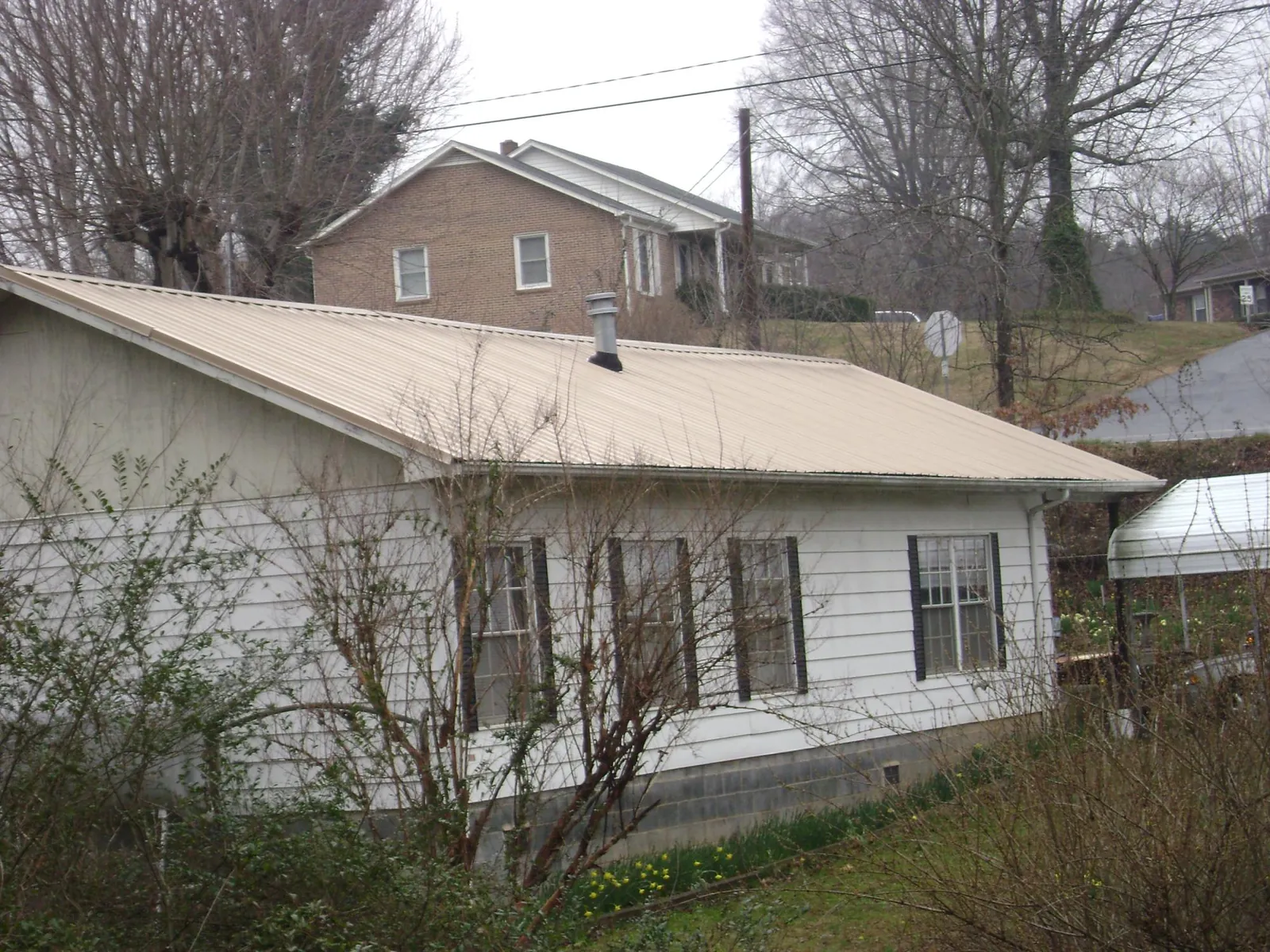 Tan metal roof on a white sided house set into a hillside — Commercial Roofing by Roofing Brothers in Pennsville